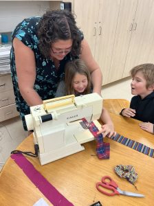 Teacher helping students use a sewing machine.